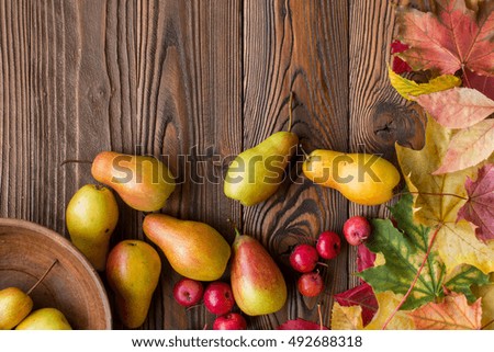 pears and red apples in clay plate, scattered with fallen leaves on wooden table. top view