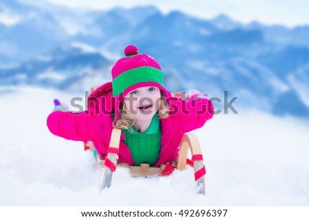 Little girl enjoying a sleigh ride. Child sledding. Toddler kid riding a sledge. Children playing outdoors in snow. Kids sled in the Alps mountains in winter. Outdoor fun for family Christmas vacation