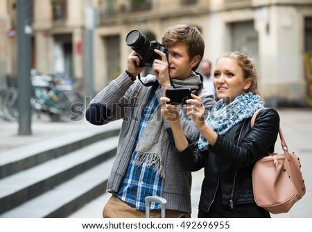 Couple of smiling young tourists making photo with digital camera and mobile phone

