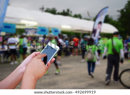 blurred image hand hold and touch screen smart phone on people riding bicycles bacground
