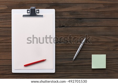 White Clipboard with Blank Paper and Office Supplies on a Wooden Background. Top View with Blank Space for Your Text