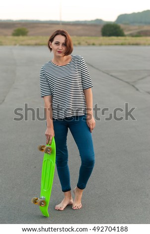 Girl standing barefoot on the asphalt with a skateboard.