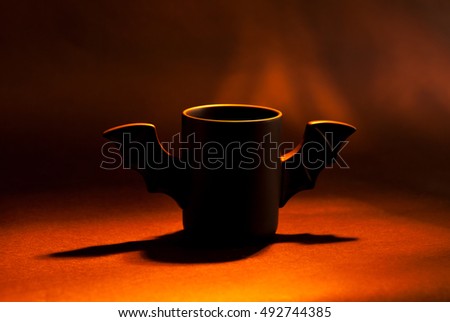 cup of coffee as bat for Halloween on black background. Red light and shadow. Toy . concept