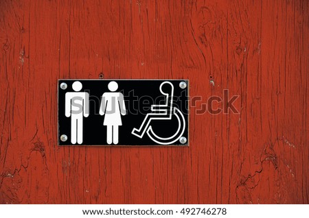 A close up image of a public washroom sign on a red building.