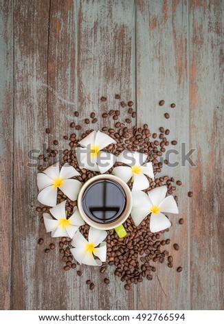 Green cup of coffee with plumeria flower and coffee bean on wood vintage background, hipster lifestyle, flat lay image and copy space