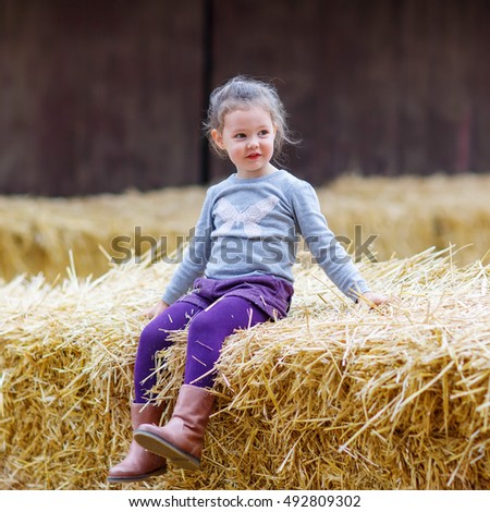 Adorable cute happy girl having fun with hay on a farm. Child enjoying autumn season and laughing. Happy childhood, lifestyle concept.