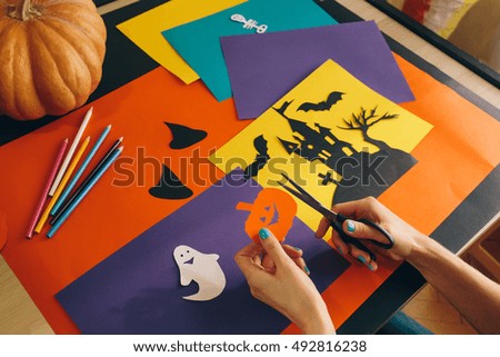 close up female hands with scissors cut paper pumpkin on the background Halloween composition. Castle, ghosts, pumpkins and other handmade spooky decorations. Halloween holiday concept. 