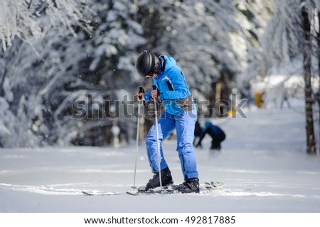 Isolated portrait of young female skier is putting on her skis on a sunny day against beautiful snow covered trees on the background. Ski resort. Bukovel, Ukraine