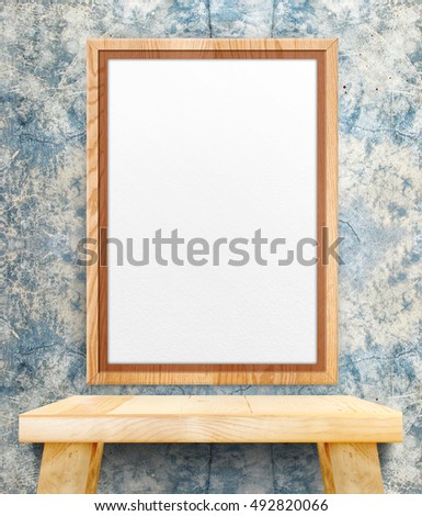 Blank wooden photo frame hanging at grunge blue concrete wall on wood table,Template Mock up for add design or text.