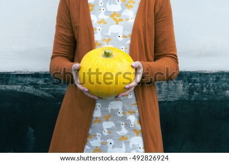 Woman holding yellow pumpkin in hands. Symbol of the holiday