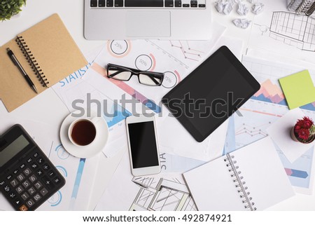 Top view of modern office workplace with blank tablet, mobile phone, laptop keypad, business reports, coffee cup and supplies. Mock up