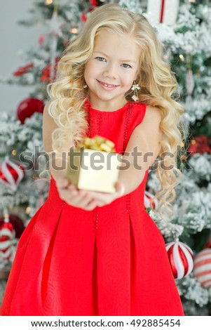 Girl delighted with gift. Child wearing a dress  next to the Christmas tree. New Year. Holiday and fun. Merry Christmas. Human emotions.