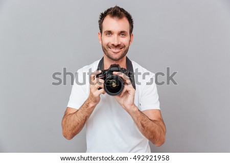 Portrait of a smiling handsome man holding camera isolated on a gray background