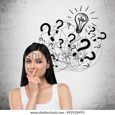 Pensive woman in white top is standing against concrete wall with multiple question marks and one light bulb. Concept of solution finding