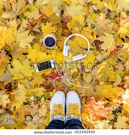 White headphones with a player and a cup of tea and coffee on a background of yellow leaves. Autumn mood. Music autumn.