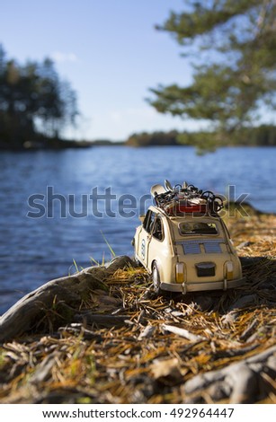 Miniature tin car traveling around the world. The car is looking out for a big lake on a sunny day. Concept image of traveling in a funny and humorous way.