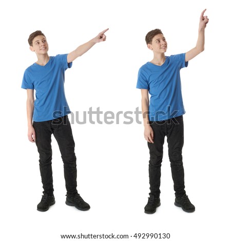 Cute teenager boy in blue T-shirt standing and poinitng up side over white isolated background full body