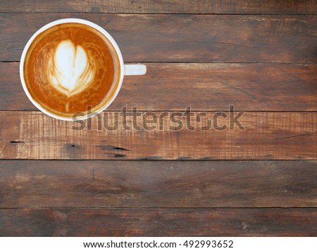 Top view of a coffee with heart pattern in a white cup on wooden plank background, latte art