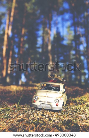 Miniature and caricature car is traveling around the world. The car is wondering across the forest on a sunny day. Image has a vintage effect applied.