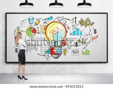 Girl with blond hair is looking at large light bulb and startup sketch on whiteboard in room with concrete walls and lamps. Concept of the next big thing