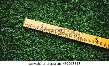 Retro styled or retro color wooden ruler with centimetre and inch indicator on green synthetic grass. Concept of land survey or mapping. Slightly de-focused and close-up shot. Copy space.