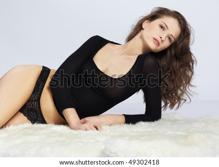 portrait of beautiful caucasian model posing on white furs in black body and panties