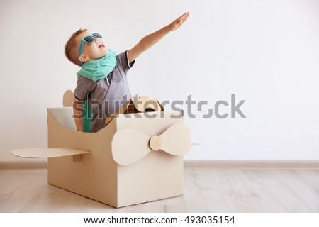 Little boy playing with cardboard airplane on white wall background Royalty-Free Stock Photo #493035154