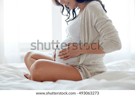 pregnancy, rest, people and expectation concept - close up of happy smiling pregnant woman sitting in bed and touching her belly at home Royalty-Free Stock Photo #493063273