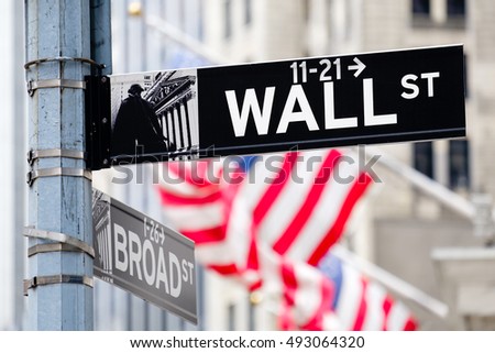Wall street sign in New York City with out of focus buildings and american flags on the background