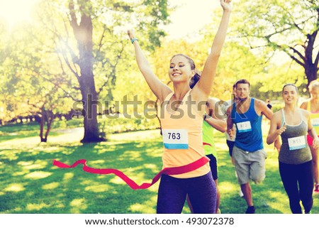 fitness, sport, victory, success and healthy lifestyle concept - happy woman winning race and coming first to finish red ribbon over group of sportsmen running marathon with badge numbers outdoors Royalty-Free Stock Photo #493072378