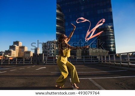 Gymnast girl with ribbon. Professional gymnast woman dancer posing with ribbon on the roof of the building. The skyscraper in the background.