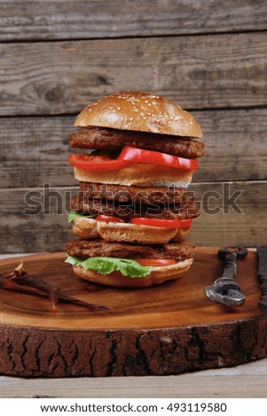 fresh grilled beef huge hamburger served on wood plate with red wine glass chili pepper rosemary green salad leaf and forged vintage antique cutlery over wooden table empty space for text