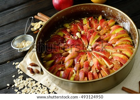 Raw traditional homemade german apple pie cake with nuts and cinnamon in form for baking on dark wooden table. Ingredients preparation recipe