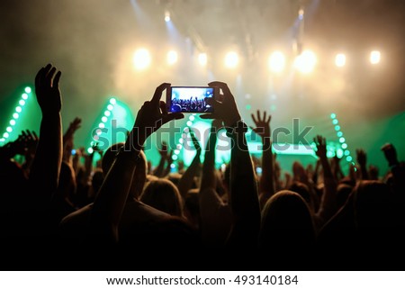 Rock concert crowd recording performance with digital smartphone, green guitar in stage