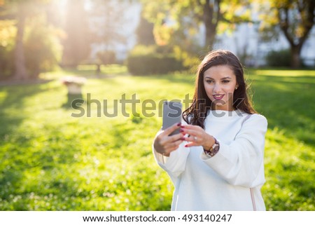 Beautiful brunette girl taking a self portrait in the park at sunset. Very shallow depth of field