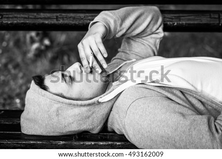 young man smoking , while lying on a bench in autumn, black and white photography
