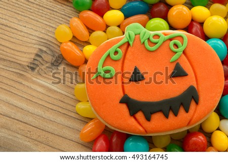 Smiling pumpkin cookie with many colorful candies on a wooden backgrund