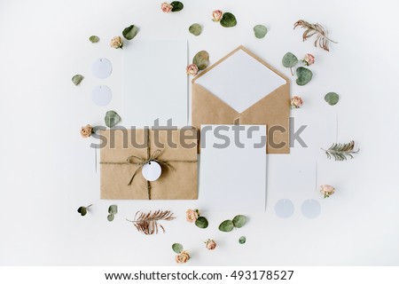 Flat lay workspace. Wedding invitation cards, craft envelopes, pink and red roses and green leaves on white background. Overhead view, top view