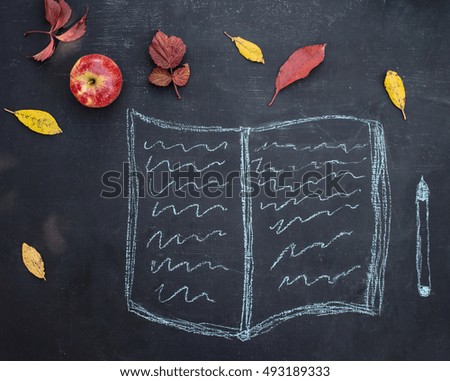 Writing pad or copybook and pen hand drawn in chalk on a blackboard with autumn leaves and apple. Back to school concept.
