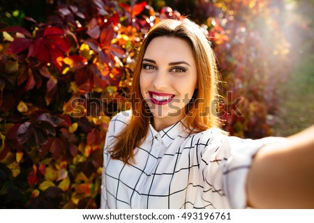 Young girl takes a selfie on the backgroung of a wall with autumn beautiful leaves.