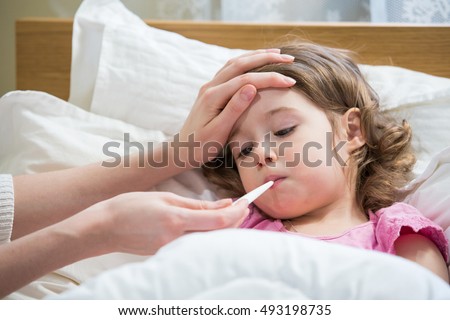 Mother measuring temperature of her ill kid. Sick child with high fever laying in bed and mother holding thermometer. Hand on forehead.  Royalty-Free Stock Photo #493198735