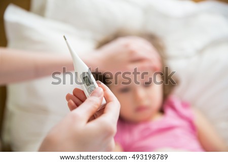 Close-up thermometer.  Mother measuring temperature of her ill kid. Sick child with high fever laying in bed and mother holding thermometer. Hand on forehead.  Royalty-Free Stock Photo #493198789
