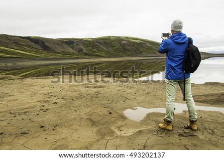 Man in Iceland on the edge of the lake photographs beautiful landscape on the phone