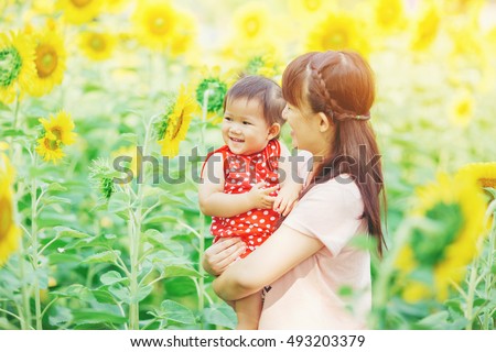 An emotional picture of 1 year old baby and her mother feeling happy together in the sun flower garden.