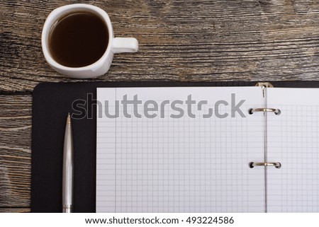 Notepad, metal pen and little white cup of coffee on wooden background