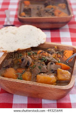 two bowls of homemade beef stew with carrots and sweet potatoes in a wooden bowl on a classic red and white checkered tablecloth
