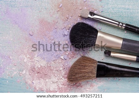 Makeup brushes on a teal blue background, with traces of powder and blush on it. A horizontal template for a makeup artist's business card or flyer design, with plenty of copyspace