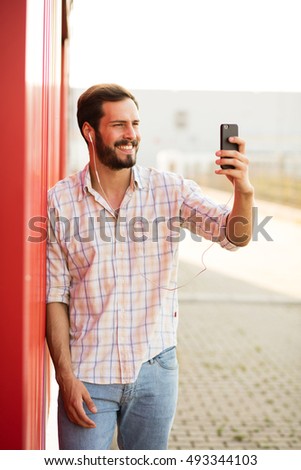 smiling man having a live cam conversation on his cellphone outside next to a red wall