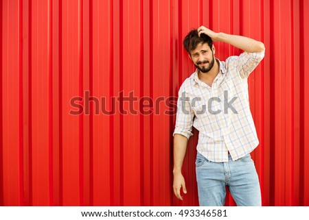 happy attractive young man smiling and playing with his hair, standing against a red wall