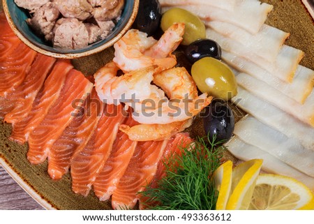 Seafood platter. Fresh cod liver, salmon, shrimp, slices fish fillet, decorated with herb, lemon and olives on light wooden background. Mediterranean appetizers. Top view